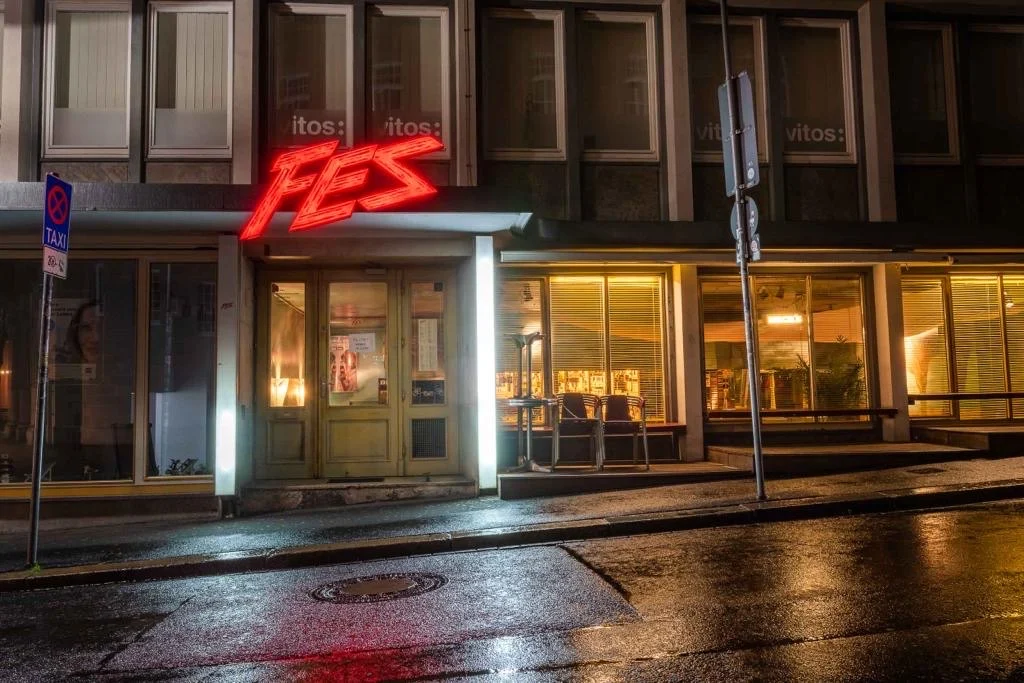 Der FES-Eingang bei Nacht mit rotem Leuchtschriftzug über der Tür.